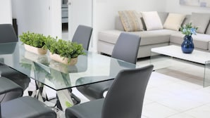 A modern living room with a glass dining table, grey sofas, and a blue vase.