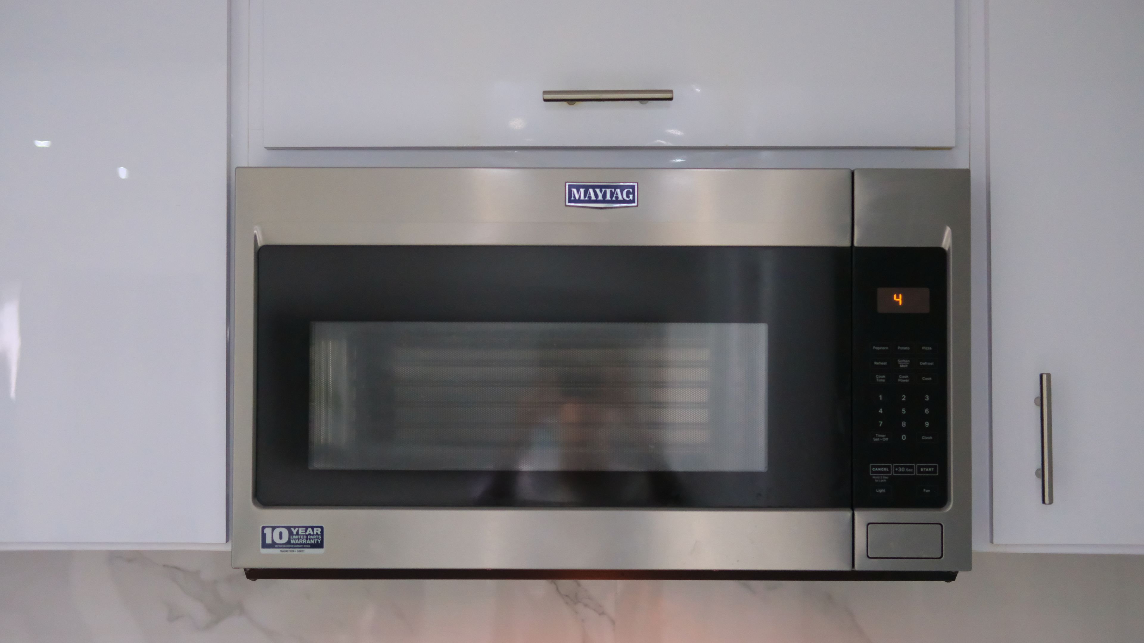 Un horno microondas Maytag de acero inoxidable con pantalla digital, una etiqueta de garantía de 10 años y un panel de control con varios botones.