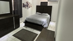 A modern bedroom with a bed, a dresser, a TV, and an air conditioning unit.