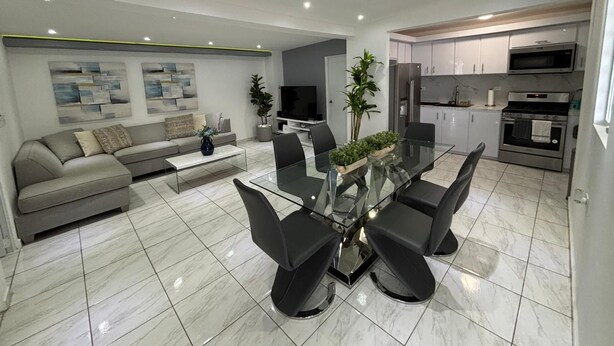 A modern living room with a sofa, coffee table, and a dining area with a glass table and chairs.