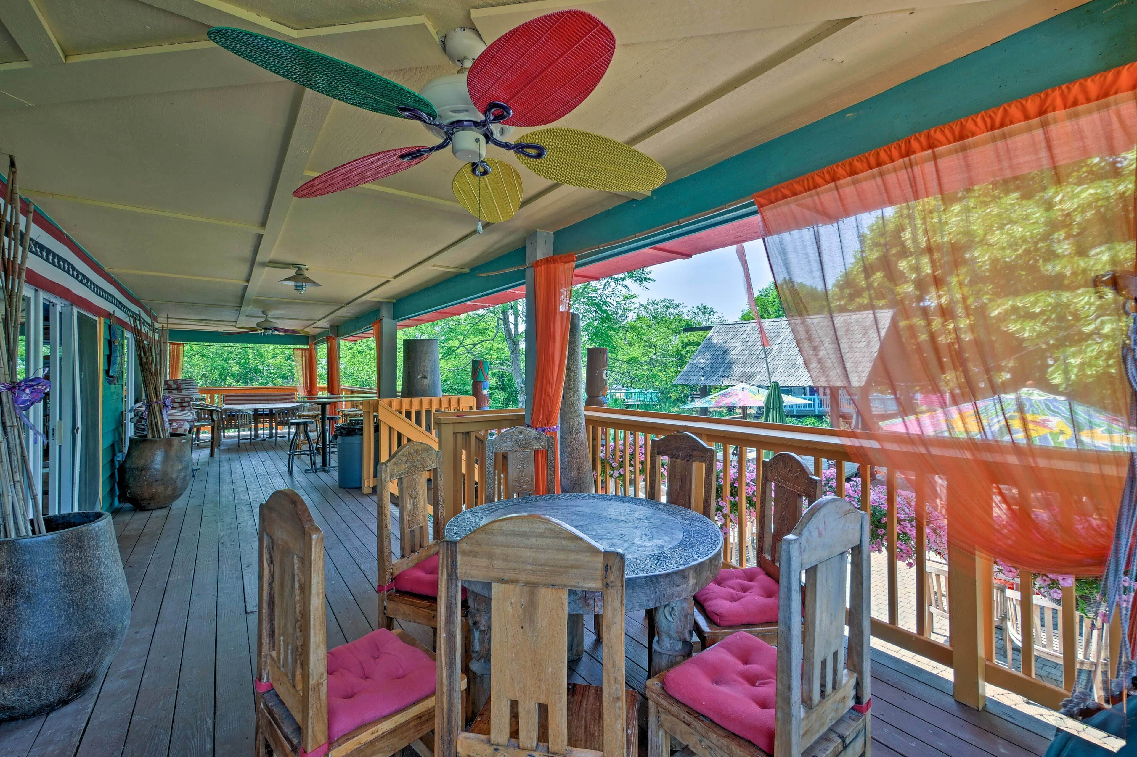 A covered outdoor area with wooden furniture, a ceiling fan, and a view of greenery.