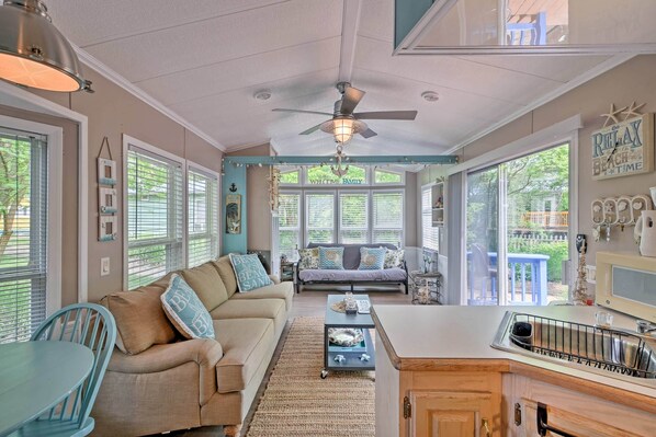 A cozy living room with a sofa, coffee table, and dining area. There are large windows and a ceiling fan. - Middle Bass Island Escape: Resort Pool & Bar! (Put-in-Bay)
