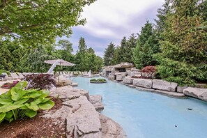 A pool area with a waterfall feature, surrounded by rocks and greenery. - Middle Bass Island Escape: Resort Pool & Bar! (Put-in-Bay)