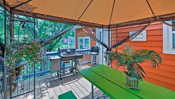 A covered outdoor area with a green table, a barbecue grill, and a hanging flower pot.