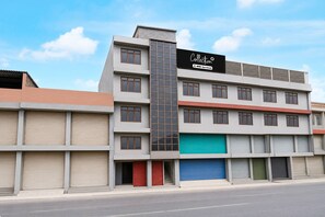 Ein mehrgeschossiges Gebäude mit einem markanten, vertikalen Abschnitt, unterschiedlichen Fenstergrößen und einer Mischung aus geschlossenen und geöffneten Läden.