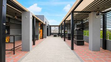 A covered outdoor area with a central pathway, benches, and tables, surrounded by walls and columns.