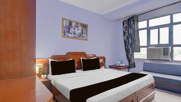 A hotel room with a bed, bedside tables, a window with curtains, a painting on the wall, and a radiator.