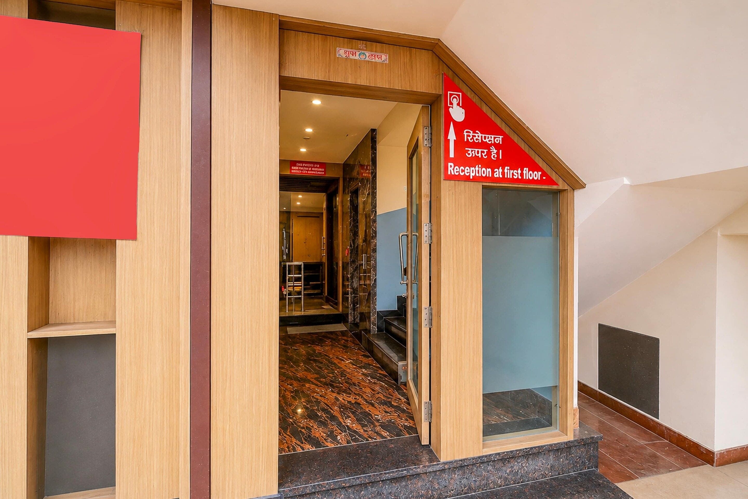 A hotel entrance with a reception desk on the first floor, a staircase leading to the upper floors, and a sign indicating the reception location.