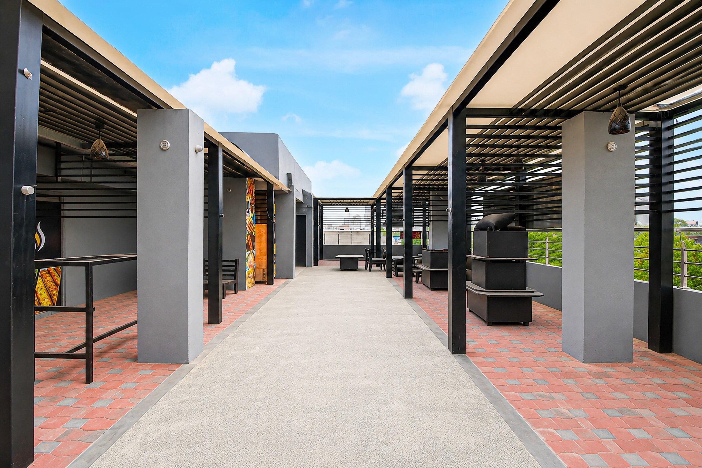 A covered outdoor area with a central pathway, benches, and tables, surrounded by walls and columns.