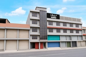 A multi-story building with a prominent vertical section, a variety of window sizes, and a mix of closed and open shuttered storefronts. - Classic Hotel Shan (Jaipur)