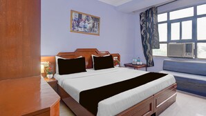 Ein Hotelzimmer mit Bett, Nachttischen, einem Fenster mit Vorhängen, einem Bild an der Wand und einem Heizkörper.