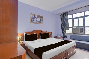 A hotel room with a bed, bedside tables, a window with curtains, a painting on the wall, and a radiator. - Classic Hotel Shan (Jaipur)