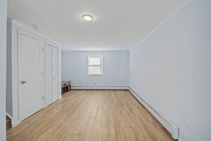 A room with a wooden floor, white walls, a window with blinds, and a door.
