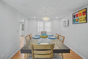 A dining room with a wooden table set for six, surrounded by chairs, a chandelier, and a large window with sheer curtains. - 3 Mi to Talcott Mtn! Family Home w/ Yard & Grill (Bloomfield)