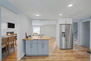 A modern kitchen with a central island, a built-in refrigerator, and a dining area with a TV above the fireplace.