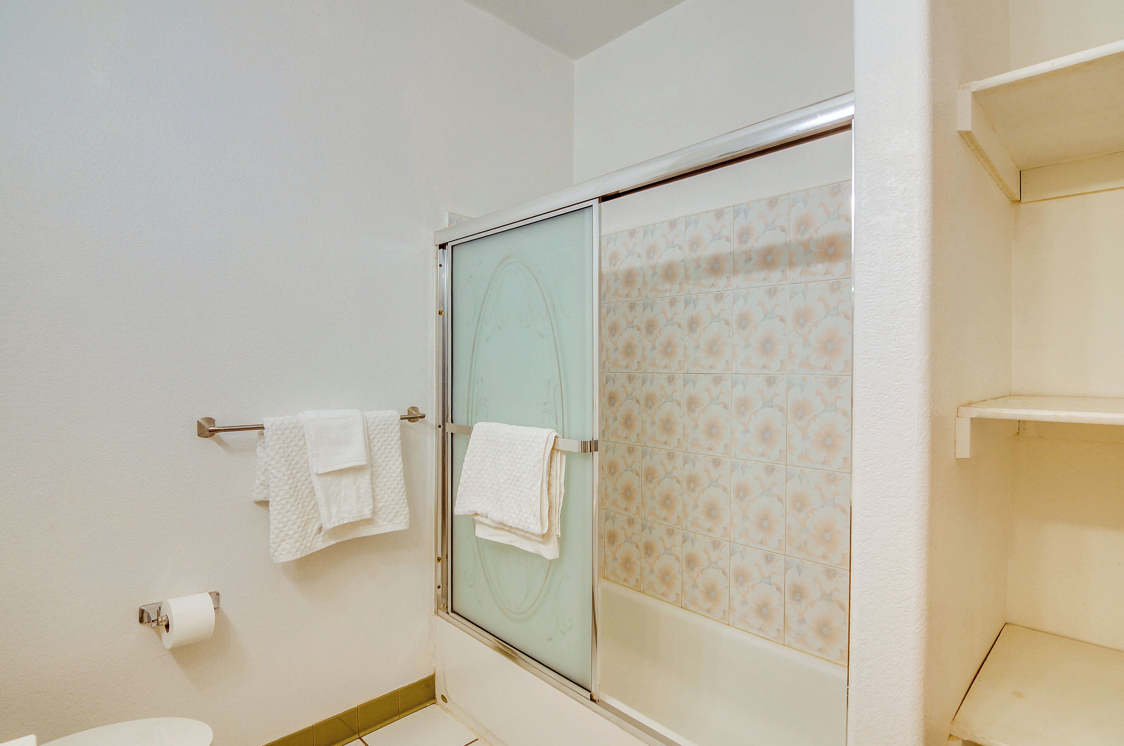 Un baño con mampara de vidrio, inodoro y toallero con toallas.