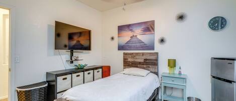 Une chambre à coucher moderne avec un lit, une télévision, un tableau, une horloge et une petite table avec une lampe.