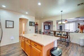 A modern kitchen with wooden cabinets, a central island, and a dining area with chairs.