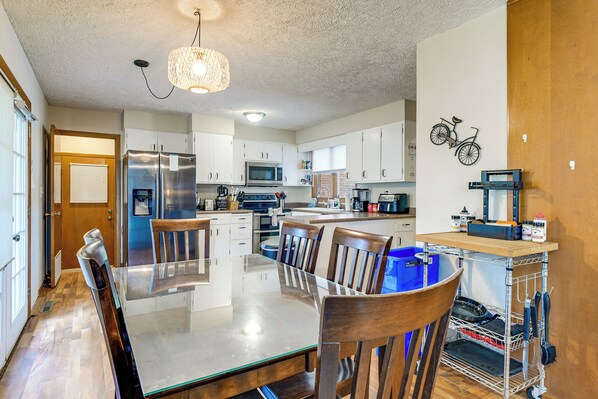 A modern kitchen with stainless steel appliances, a dining area with a glass table, and a wall-mounted bicycle decoration.