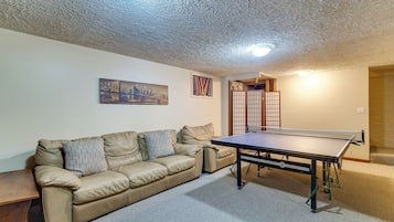 A room with a sofa, a ping pong table, and a cityscape painting.