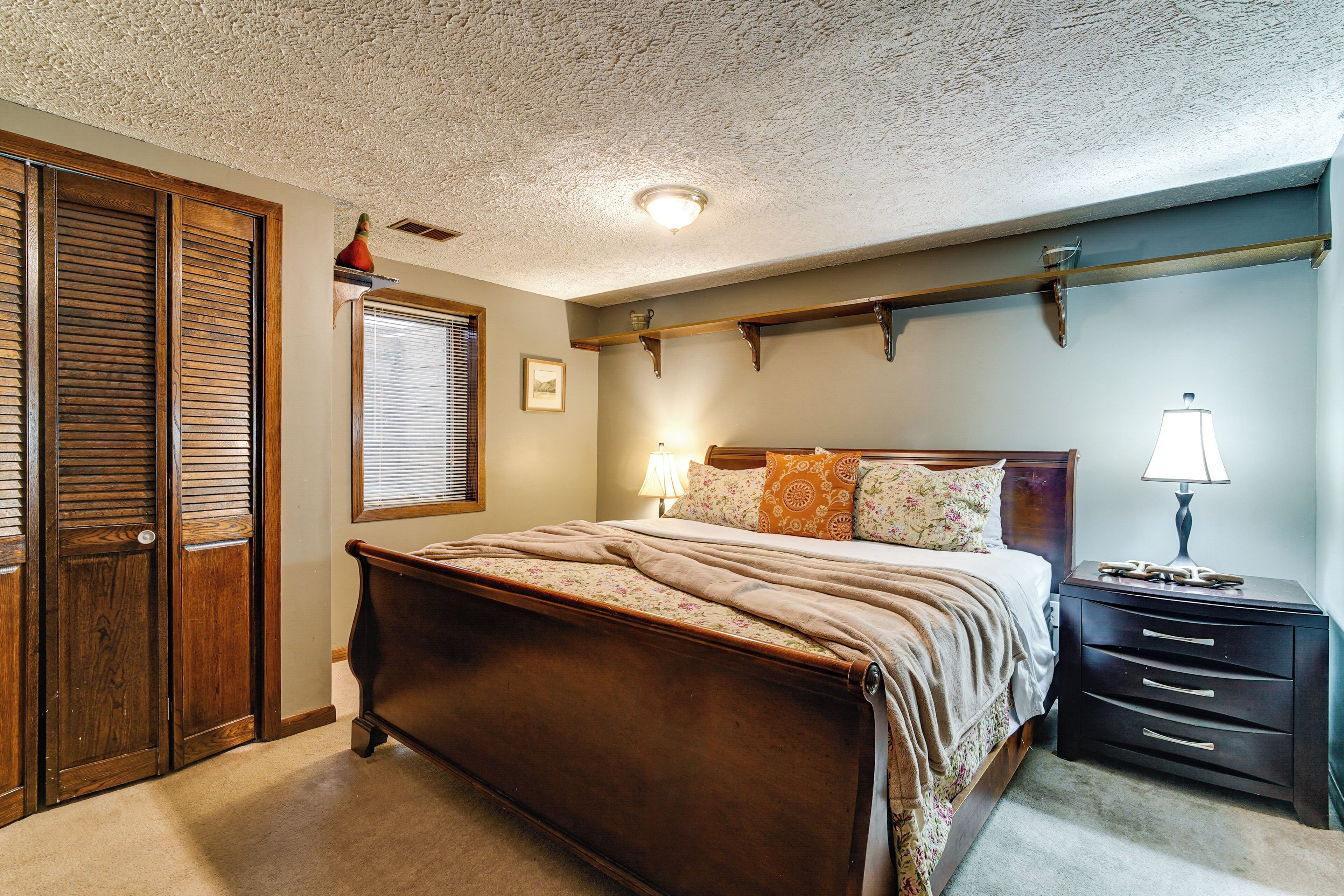 Une chambre à coucher avec un lit en bois, une table de chevet avec une lampe, une commode et un placard avec des portes coulissantes.