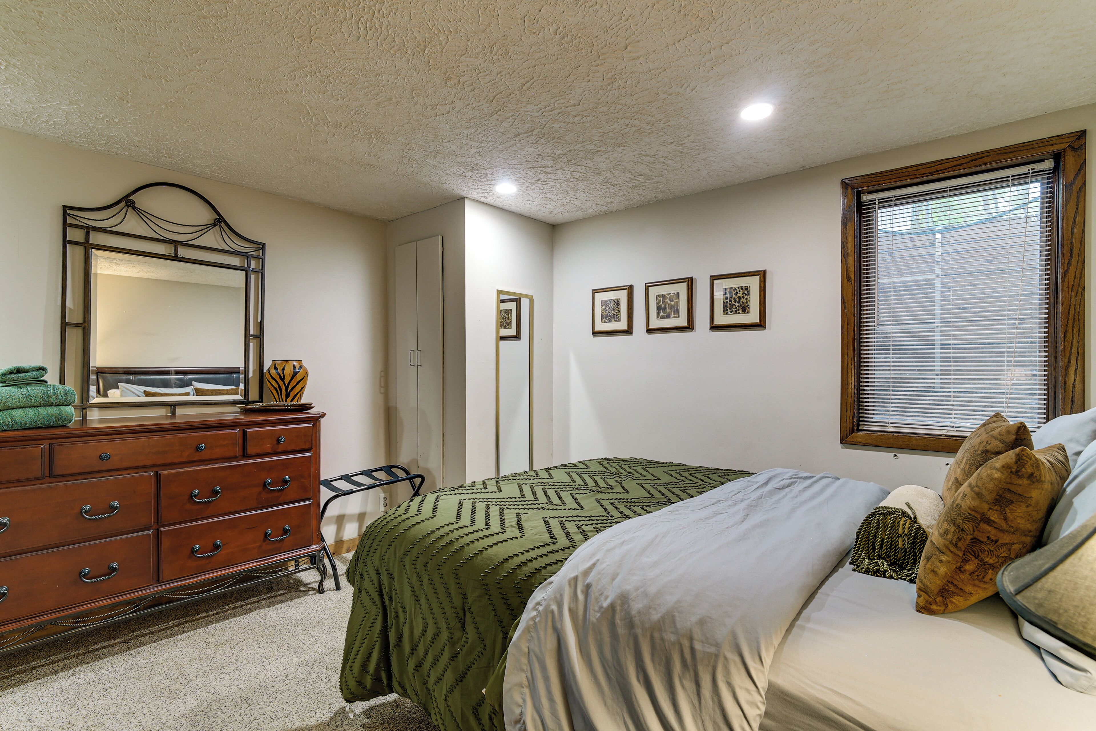 Une chambre à coucher avec un lit, une commode, un miroir et des tableaux encadrés accrochés au mur.