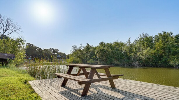 Una mesa de picnic de madera en un muelle, con agua y árboles al fondo.