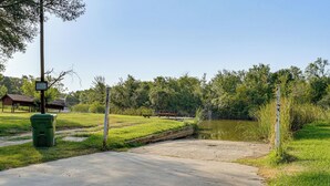 Un sendero de concreto lleva a una pequeña construcción de madera, una mesa de picnic y un cartel en un parque.