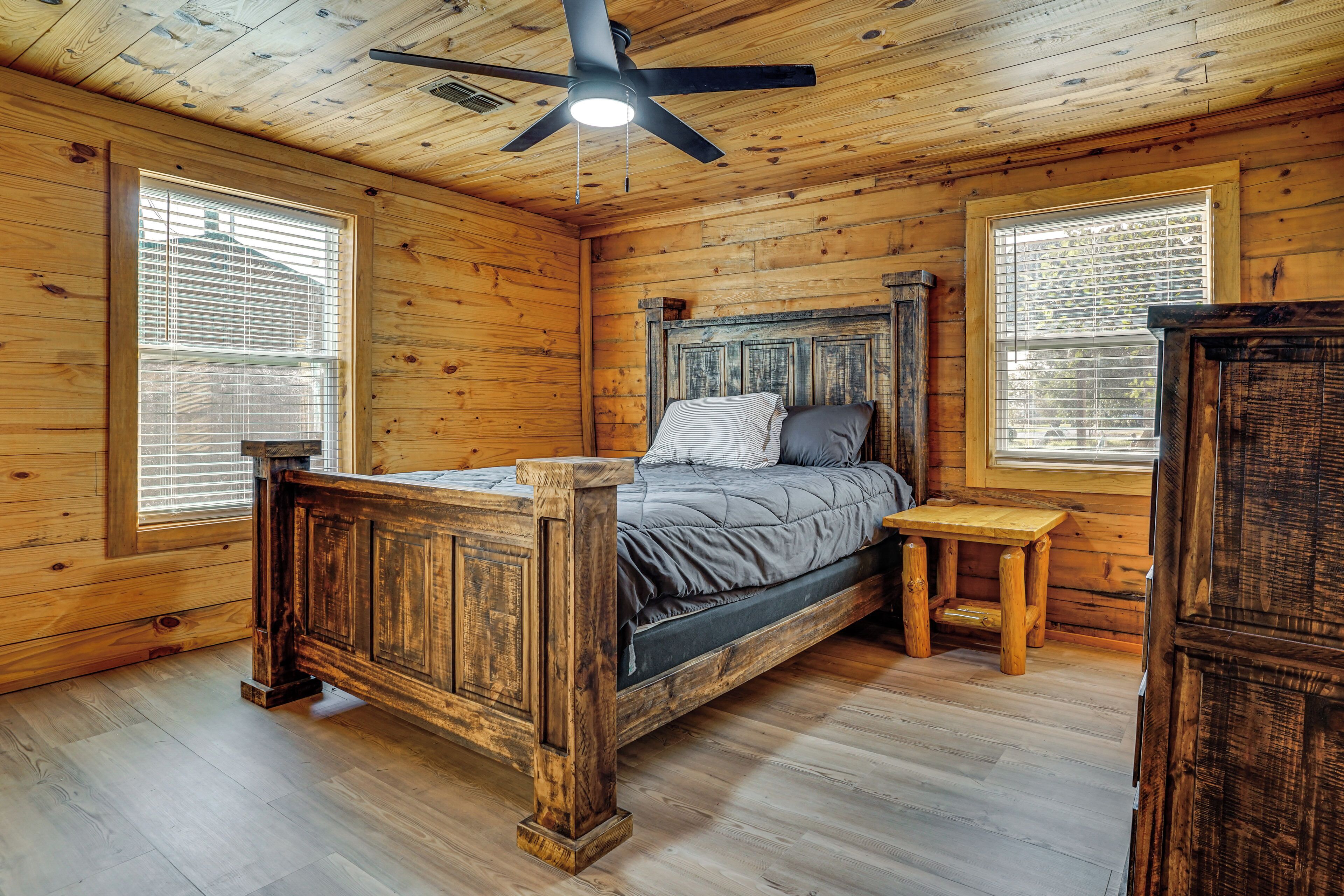 Een houten kamer met een bed, een tafeltje en een plafondventilator.