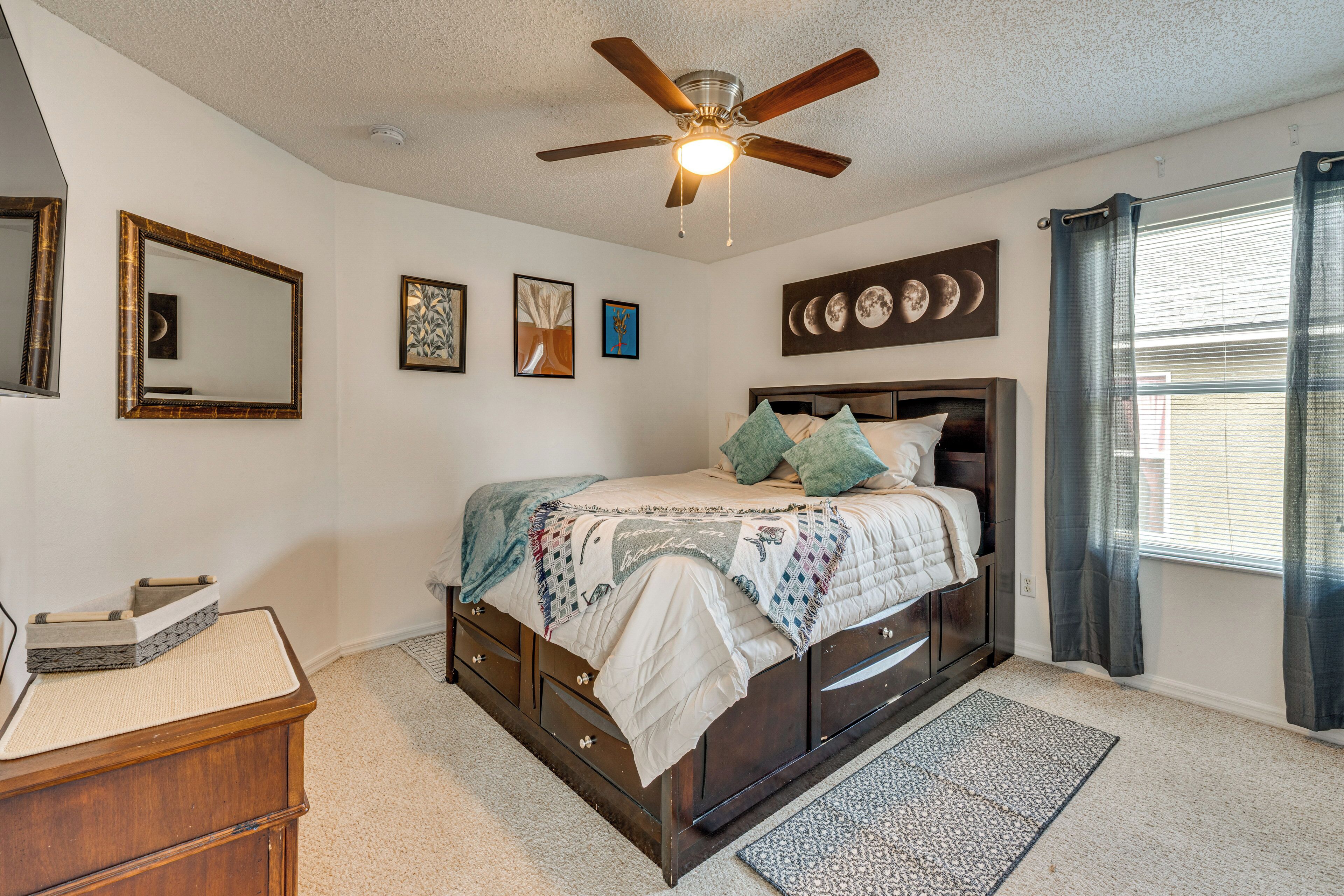 Quarto com cama, ventilador de teto, janela com cortinas e decoração nas paredes.