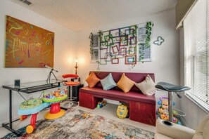 A room with a red sofa, colorful toys, a glass table, and a large abstract painting. - 9 Mi to Disney! Family-friendly Home w/ Pool (Kissimmee)