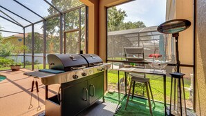 Eine überdachte Außenküche mit Grill, Tisch und Stühlen sowie ein großes Fenster mit Blick auf einen Garten.