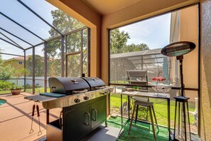 A covered outdoor kitchen with a grill, a table with chairs, and a large window overlooking a backyard. - 9 Mi to Disney! Family-friendly Home w/ Pool (Kissimmee)