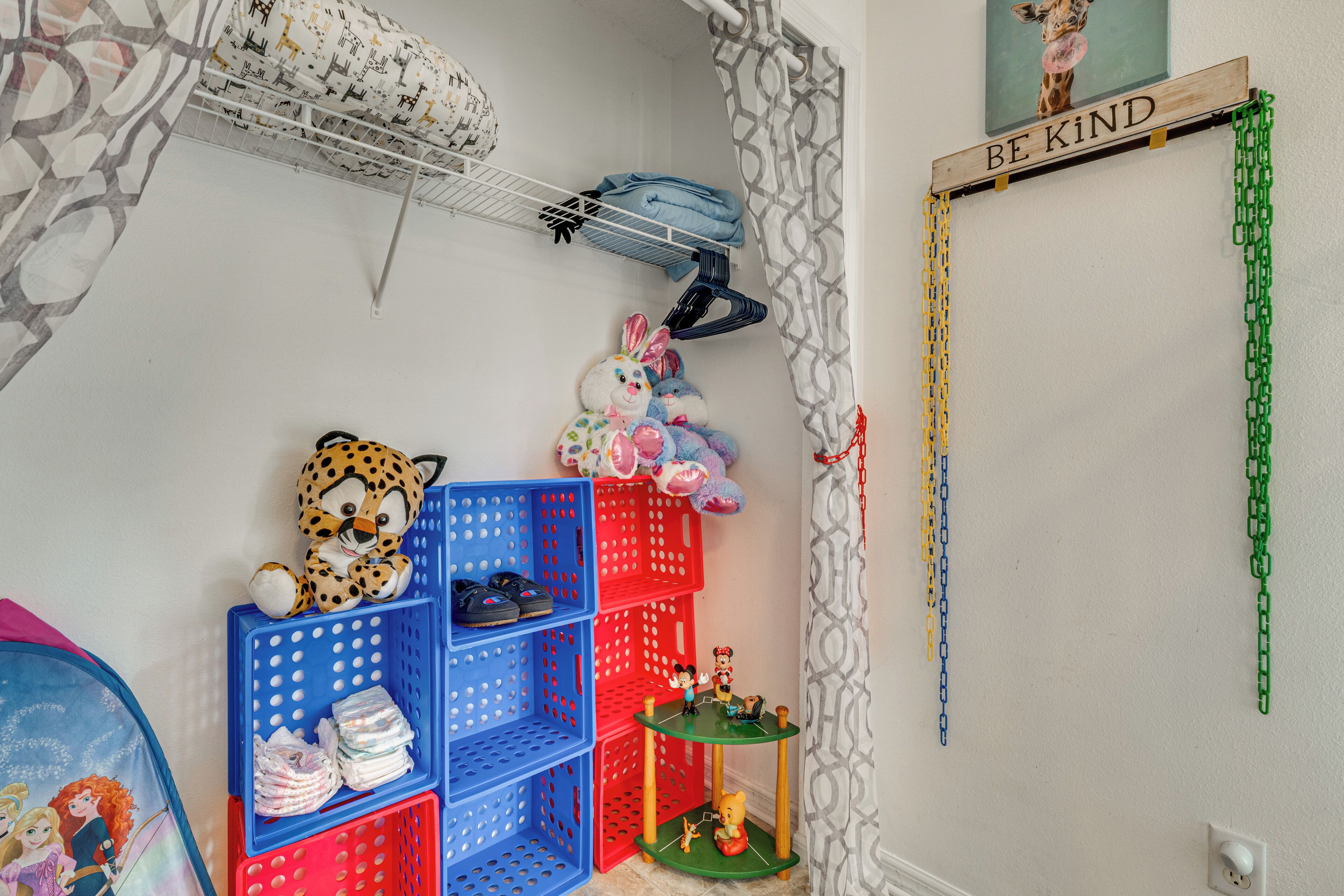 A child's room with a leopard plush toy, a giraffe wall art, and a 'BE KIND' sign.