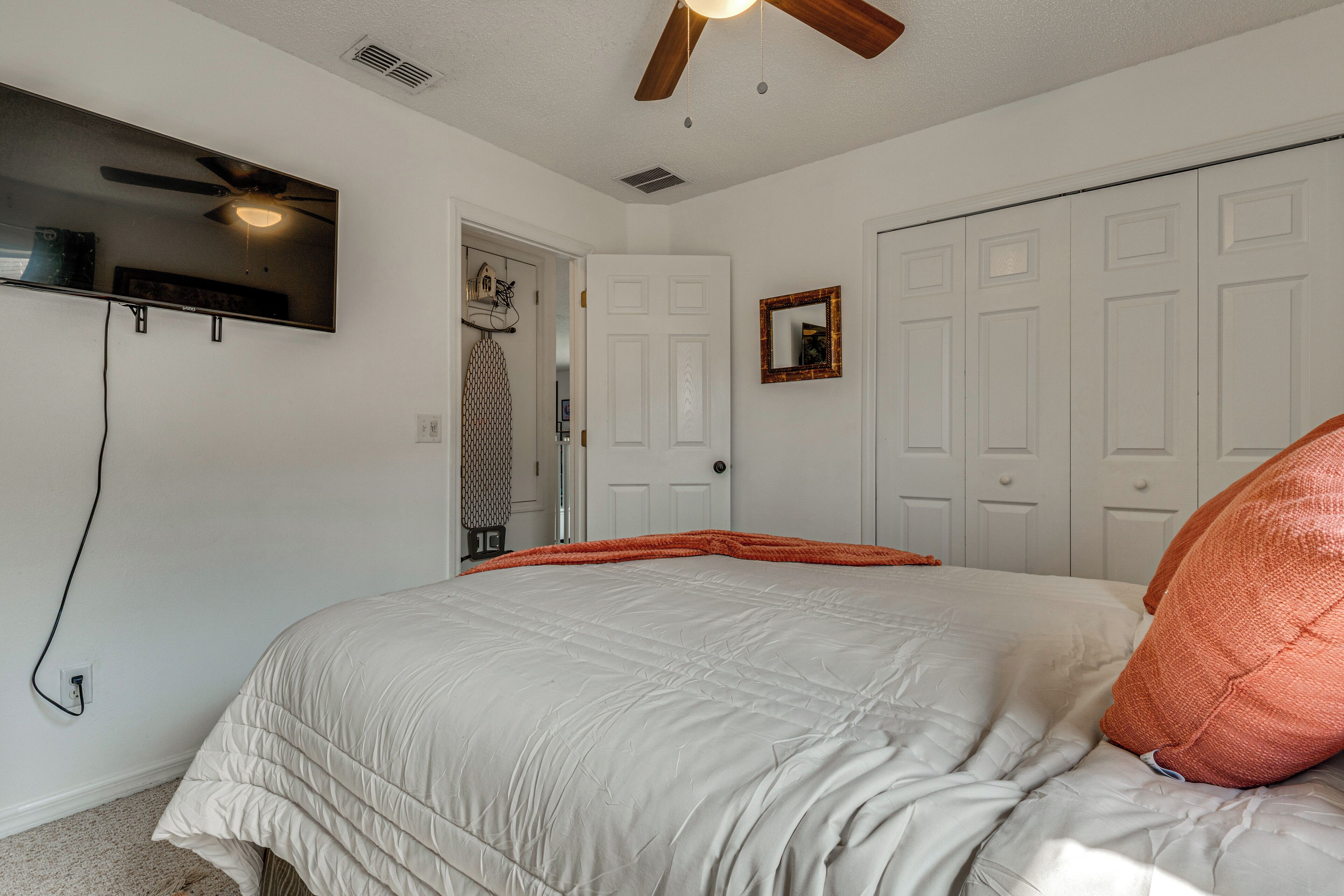 Quarto com cama, ventilador de teto, televisão na parede e uma porta.