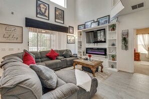 Una sala de estar con un sofá gris, cojines rojos, una mesa de centro y un televisor de pantalla plana sobre un mueble blanco.