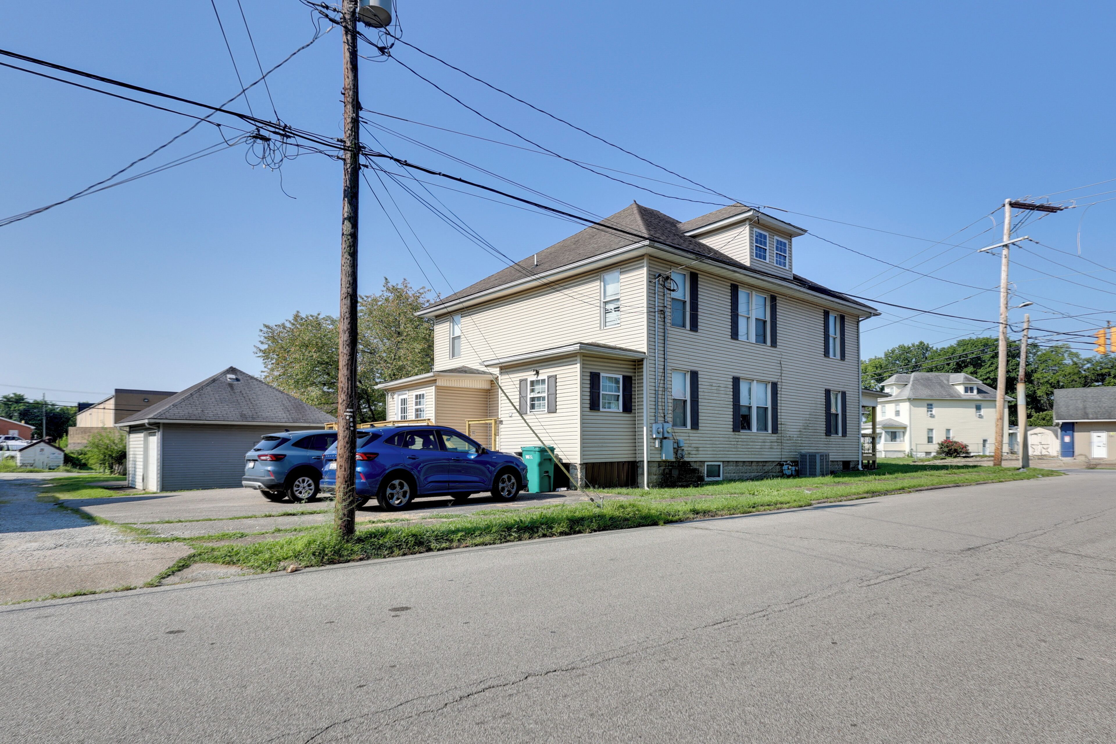 A two-story residential building with a garage, a parked blue SUV, and visible power lines.