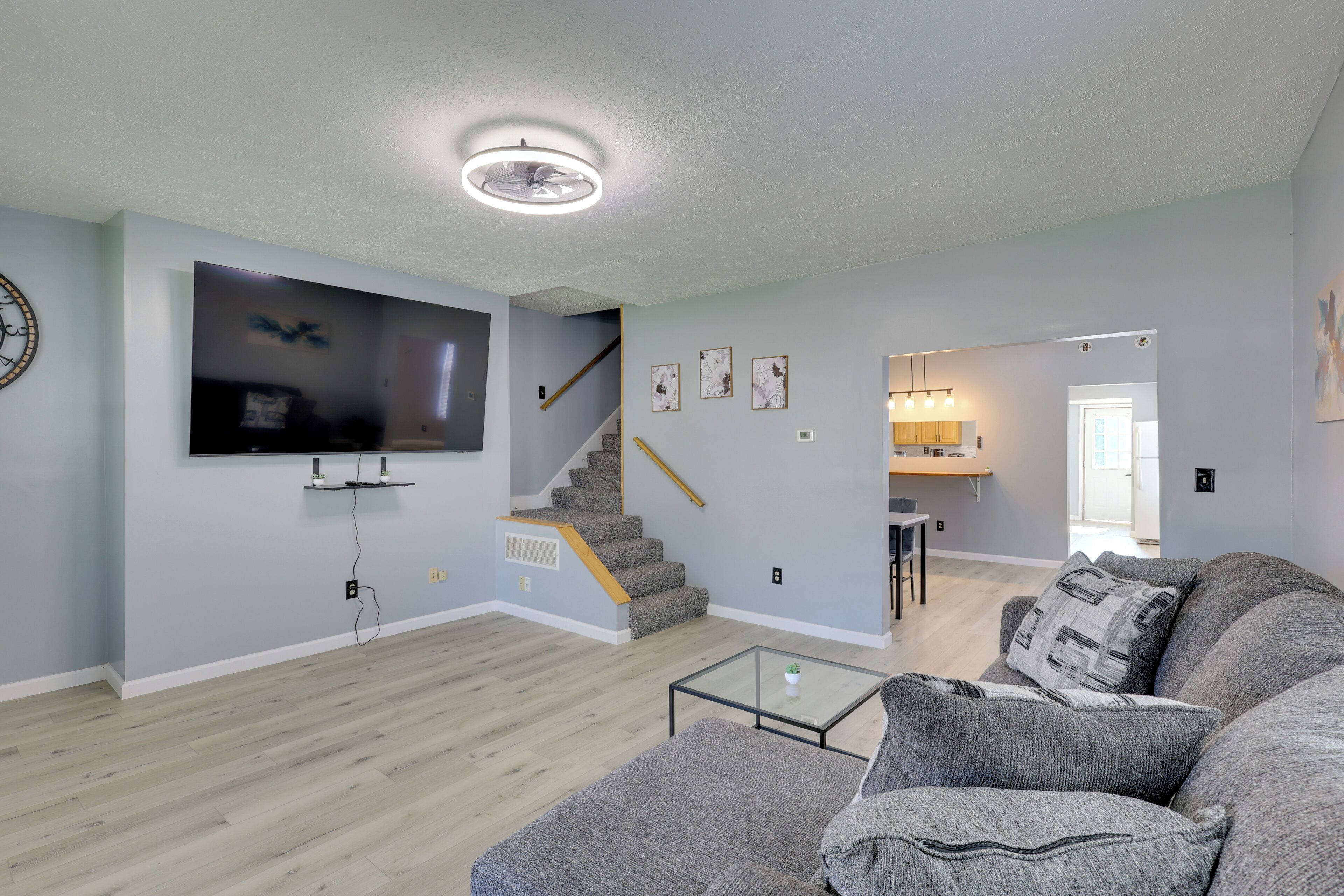 A modern living room with a flat-screen TV, a staircase, and a kitchen area.