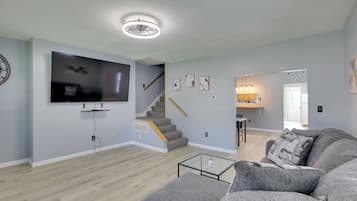 A modern living room with a flat-screen TV, a staircase, and a kitchen area.