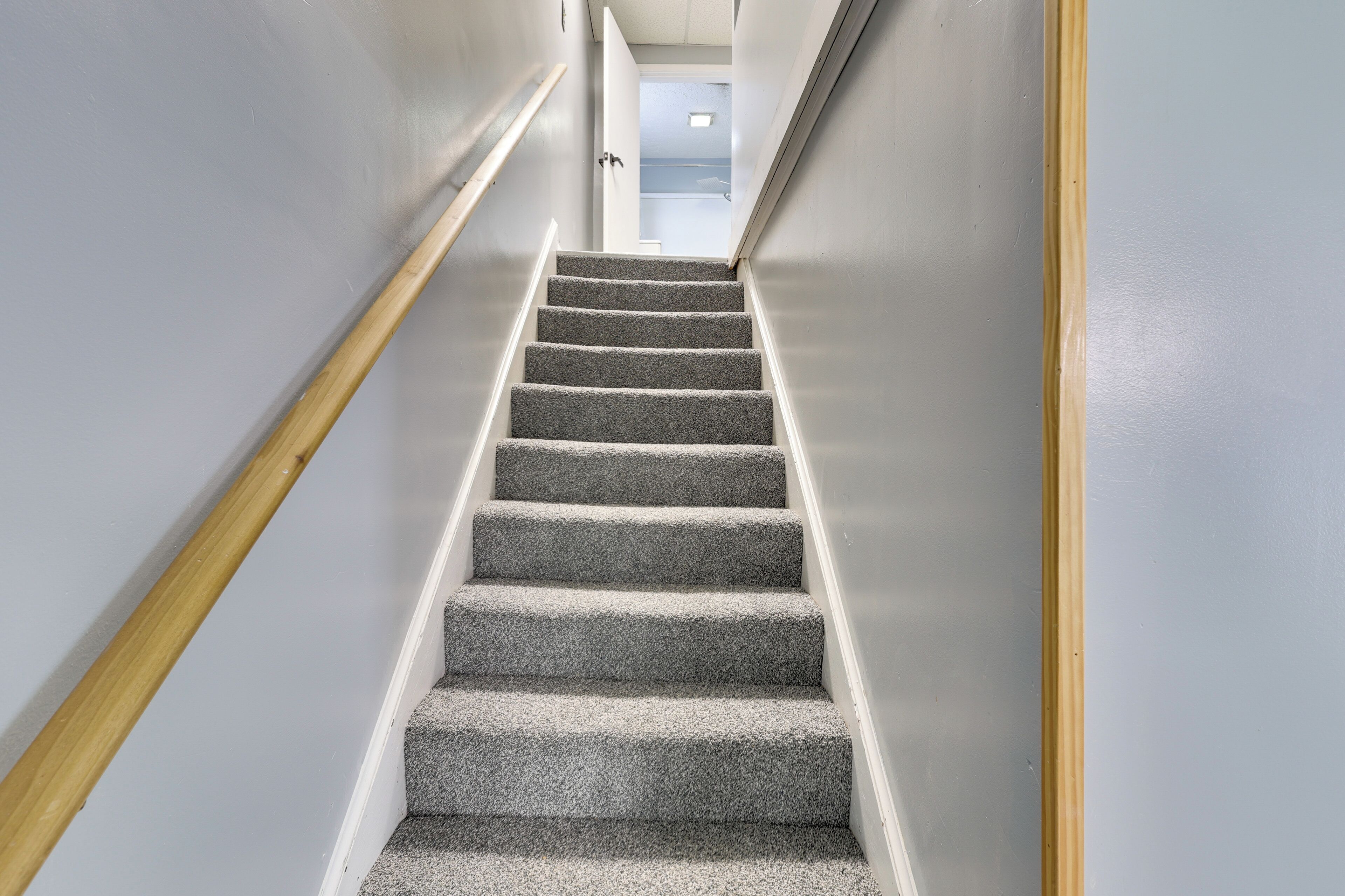 A carpeted staircase with a wooden handrail and white walls.