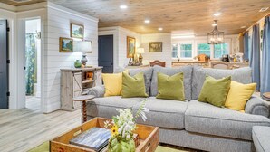 A cozy living room with a grey sofa, wooden ceiling, and a kitchen in the background. - < 1/2 Mi to Lake Burton! Forest-view Sanctuary (Clarkesville)