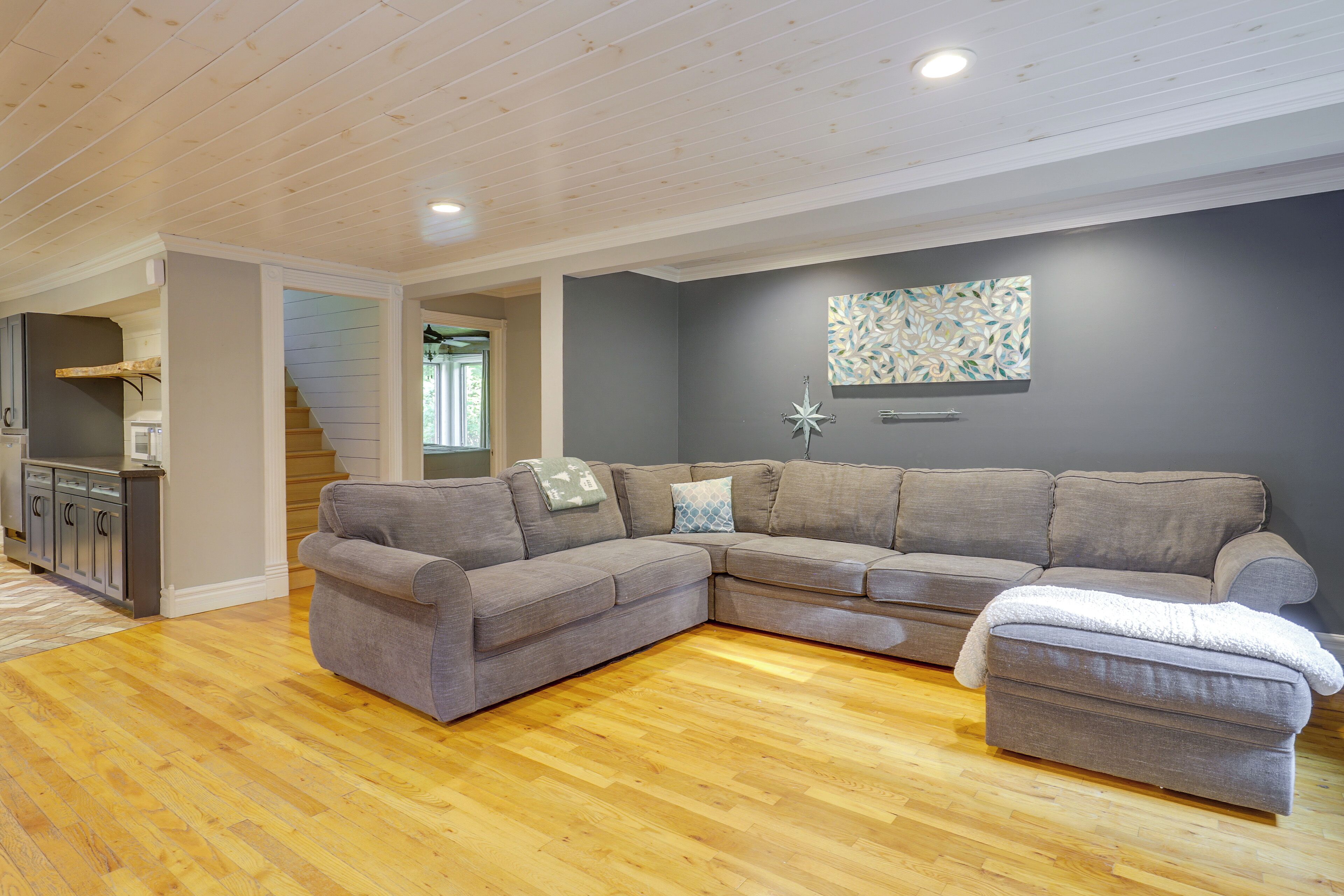 A living room with a sectional sofa, a small ottoman, and a wooden floor.