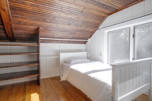 Une chambre avec un plafond en pente, un lit, une fenêtre et une échelle en bois.