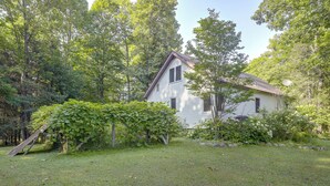 Ein Haus mit geneigtem Dach, umgeben von einem grünen Rasen und dichten Bäumen.