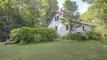 A house with a sloped roof, surrounded by a grassy yard and dense trees.