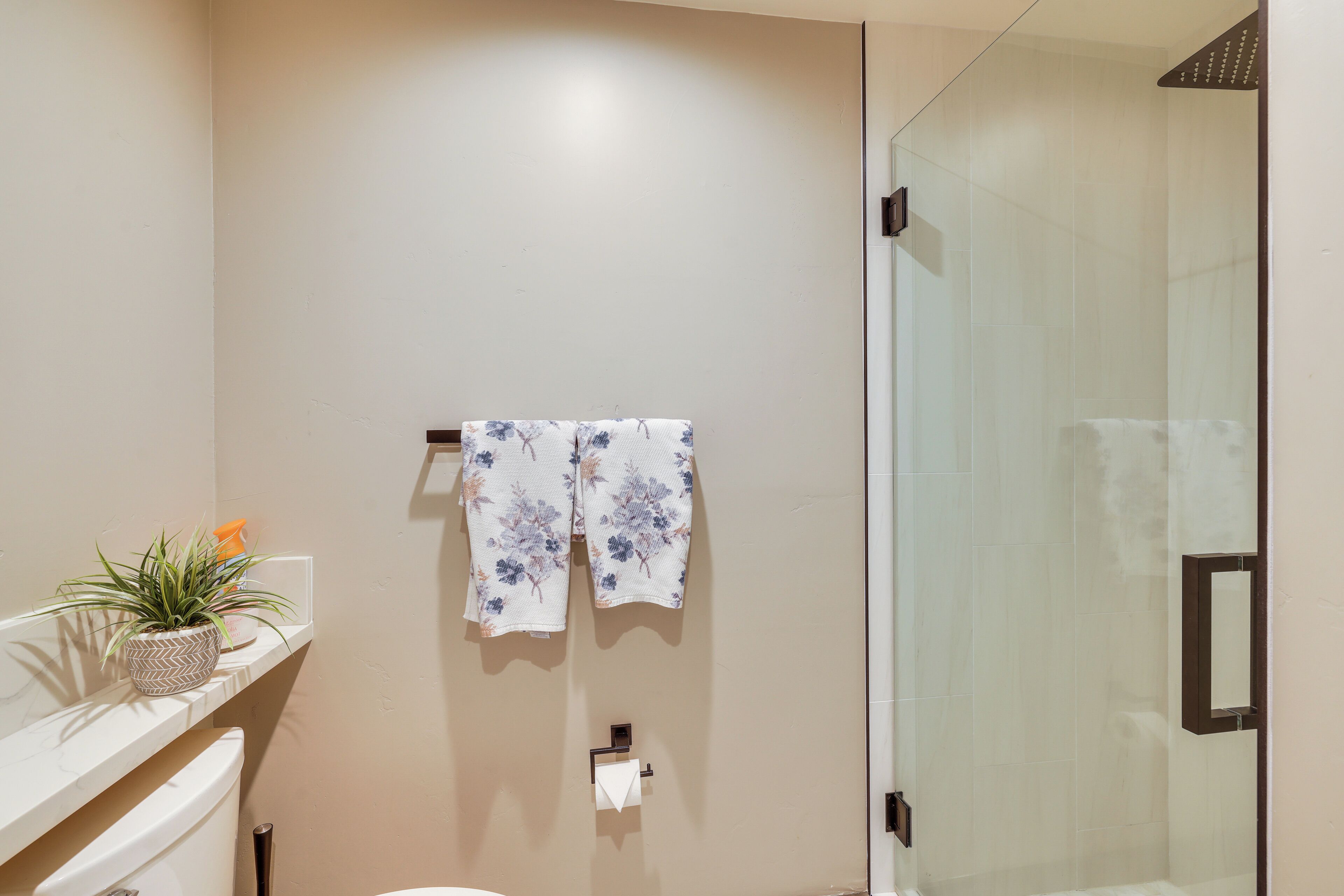 A bathroom with a glass shower enclosure, a toilet, and a towel rack with two towels.