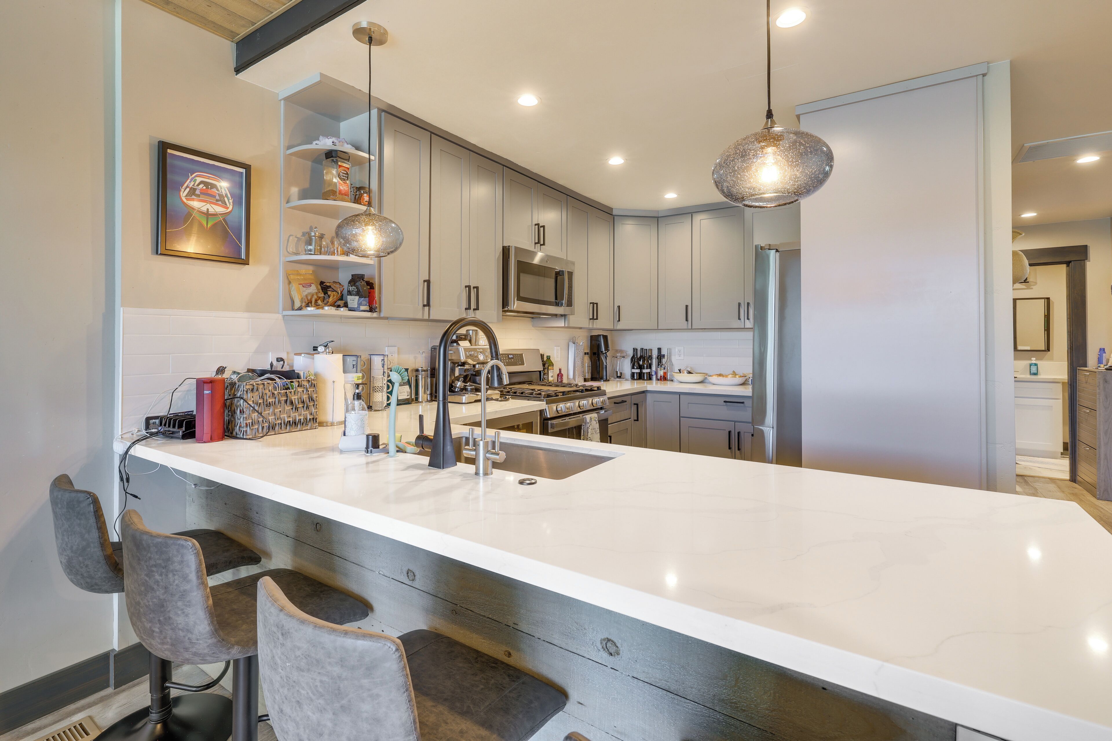 A modern kitchen with a large island, bar stools, stainless steel appliances, and pendant lighting.