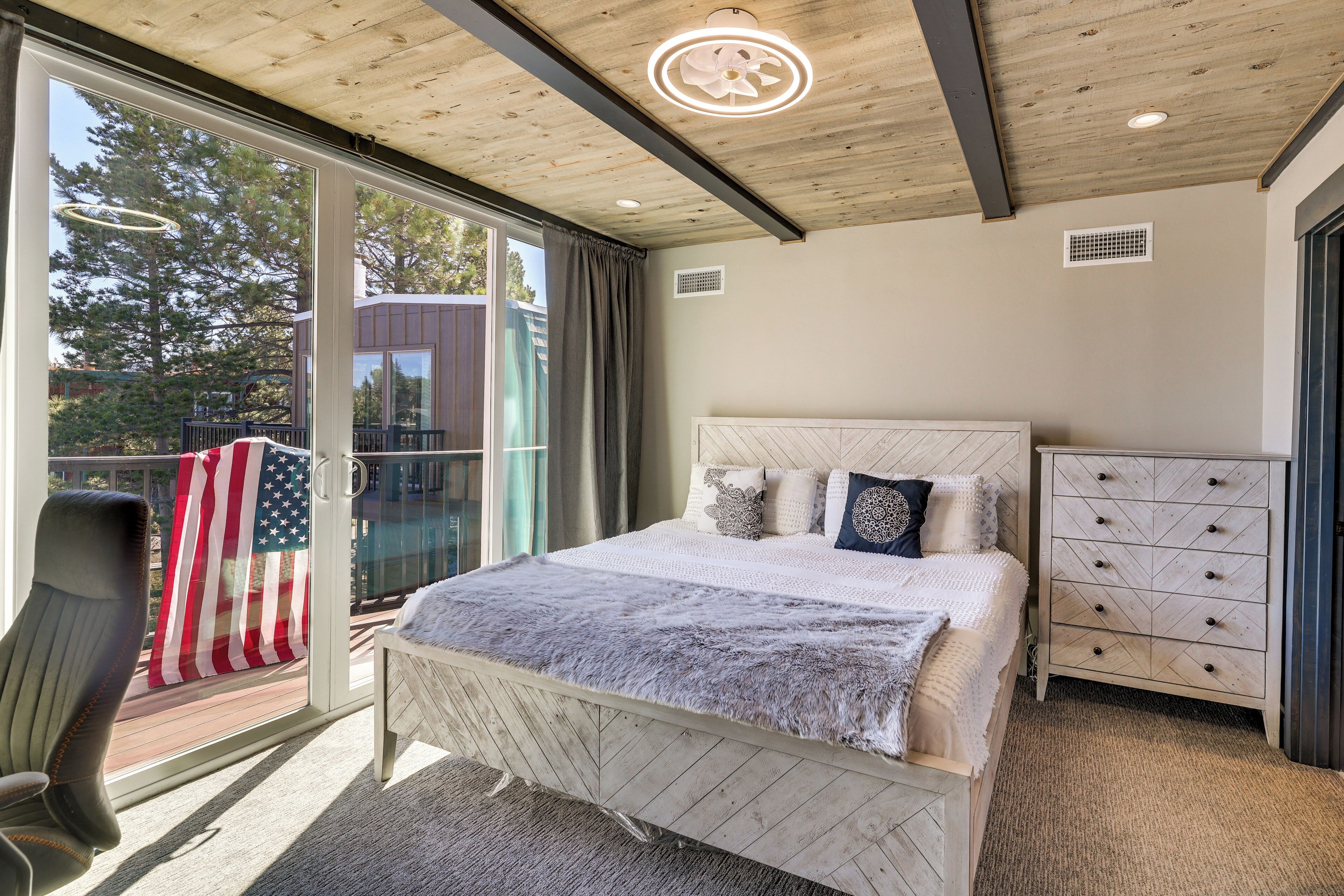A bedroom with a bed, a dresser, a chair, and a large window with an American flag.