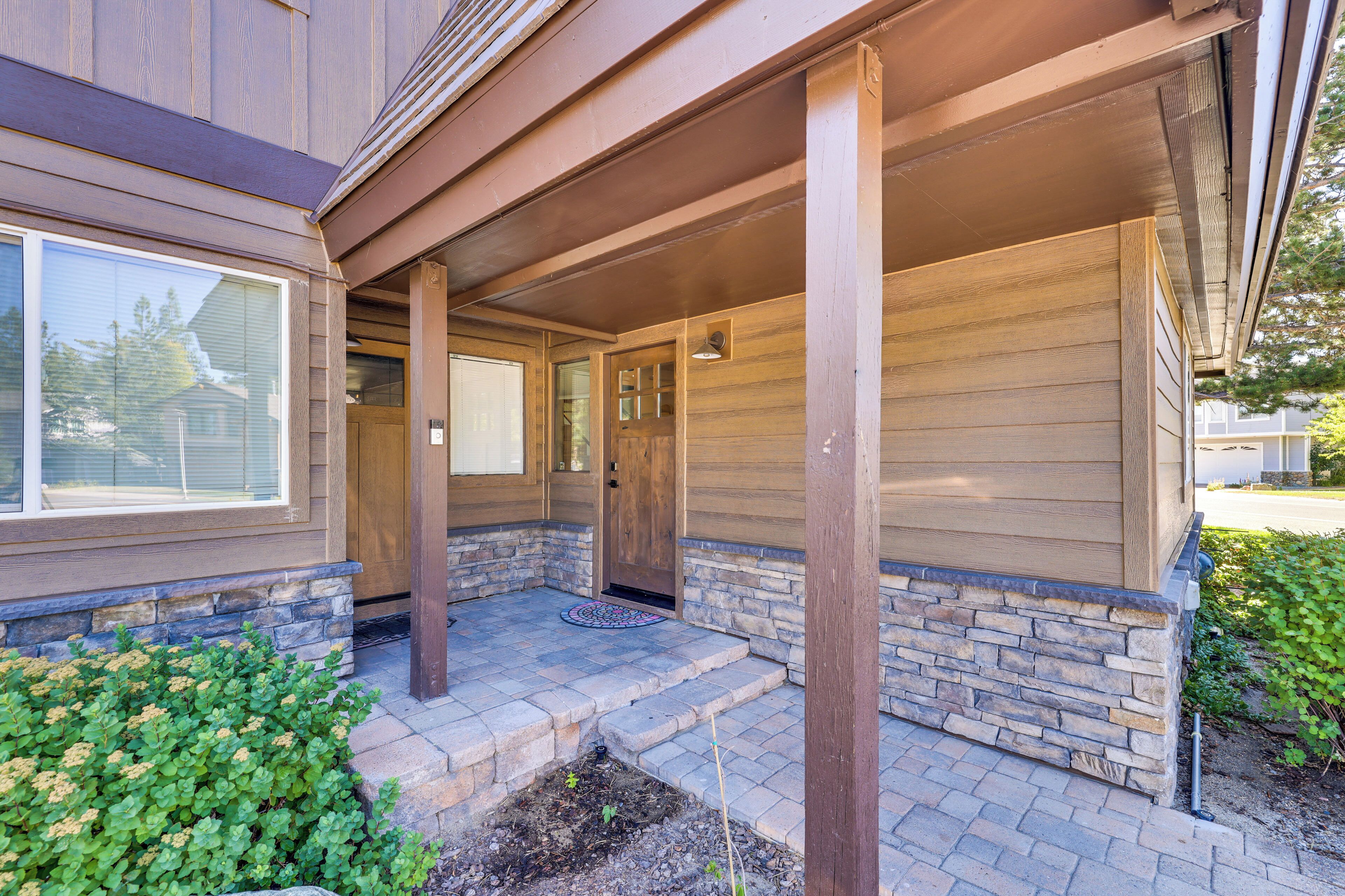 A covered porch with stone steps leading to a wooden door, surrounded by greenery.