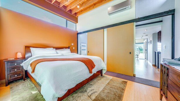 A modern bedroom with a large bed, wooden headboard, and a nightstand with a lamp. - 1/2 Mi to Alki Beach + Puget Sound Views! (Seattle)